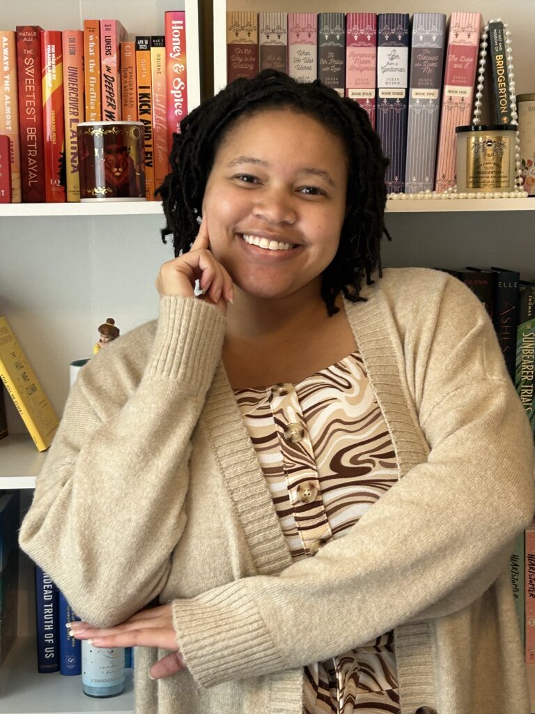 Picture of Alexia, a lightskin Black woman with black locs smiling and posing in front of two bookcases.